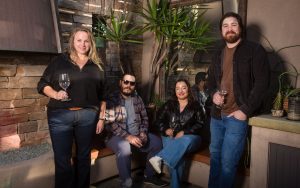 Four people pose for photo while holding wine glasses